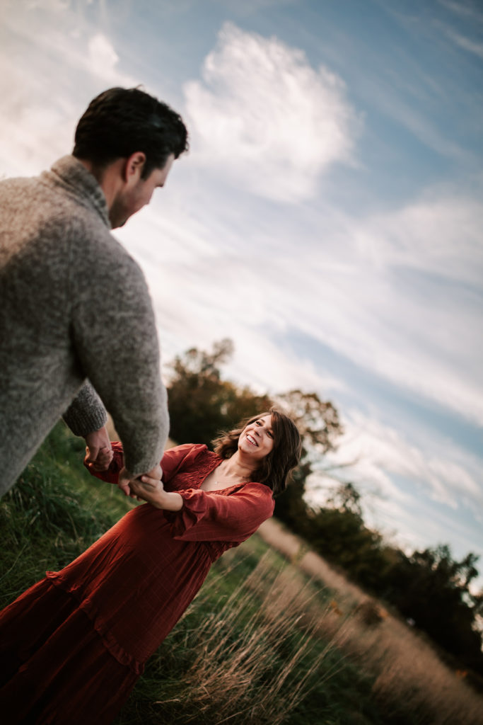 Kristen and Greg holding both hands arms stretched out, smiling at each other, in a grassy field.