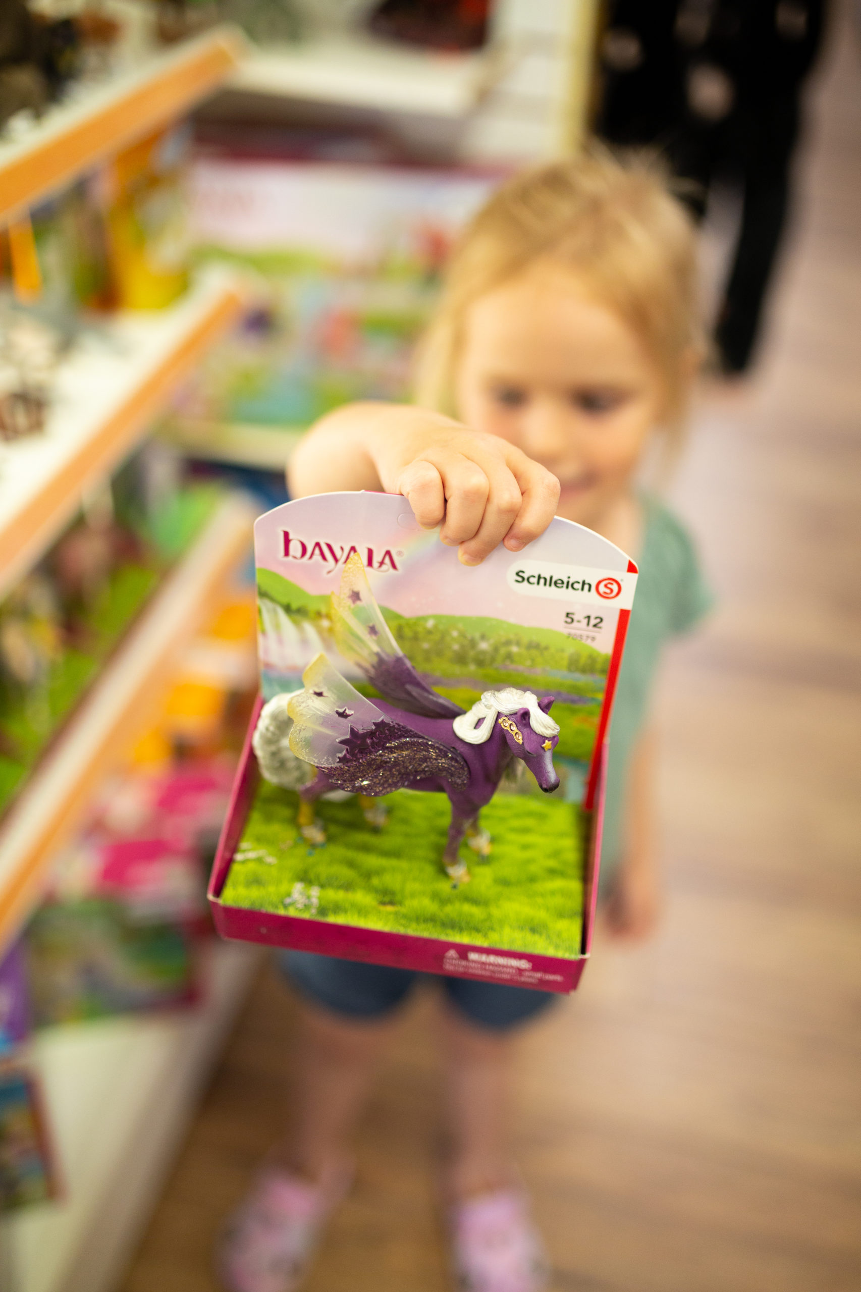 Little girl holding up a Schleich pegasus toy at Minds Alive toy store in Collingwood