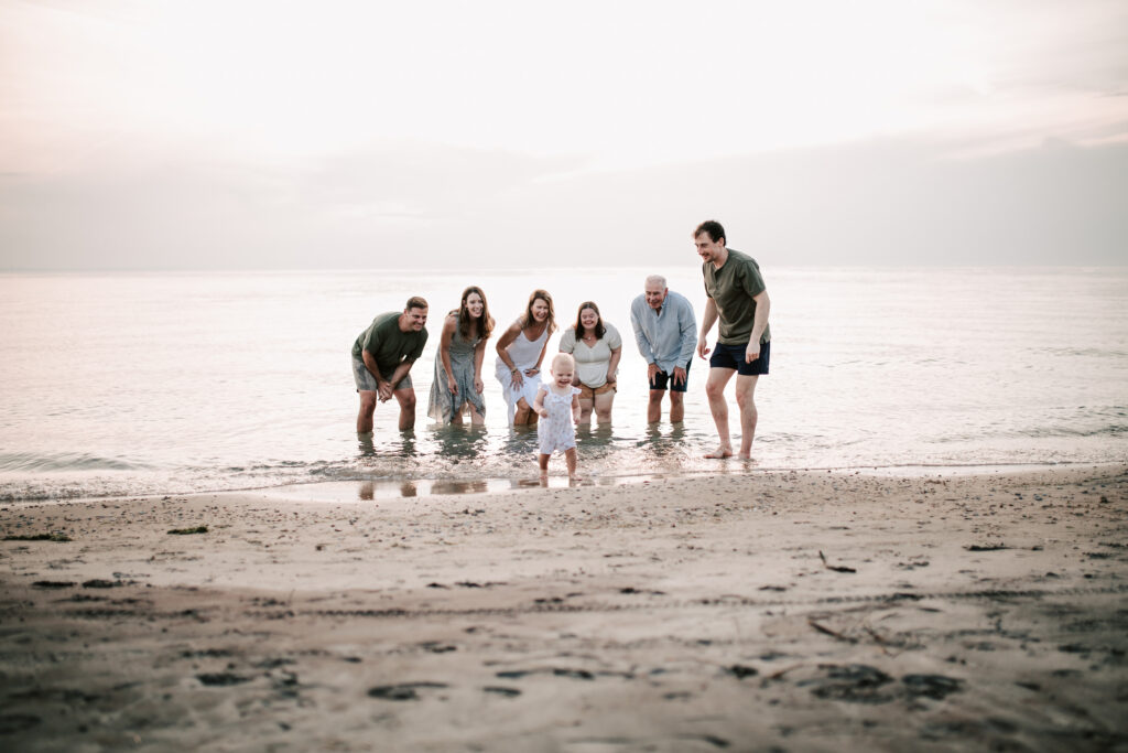 Young child running playing with extended family at a beach during candid family photography session in Tiny, Ontario