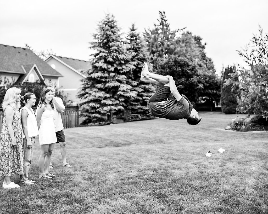 Teenage boy doing a backflip at an extended family laughing and acting silly together during outdoor family photo session near Collingwood Ontario