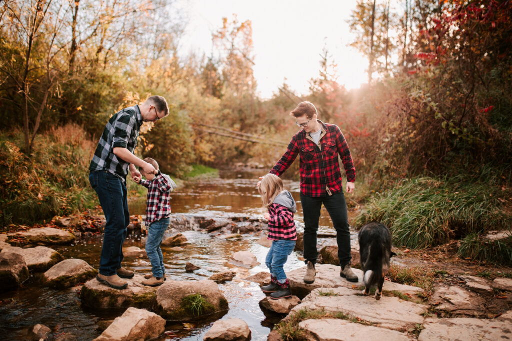 Family with two young kids exploring a creek with their dog during a full family session near Collingwood, Ontario at golden hour.